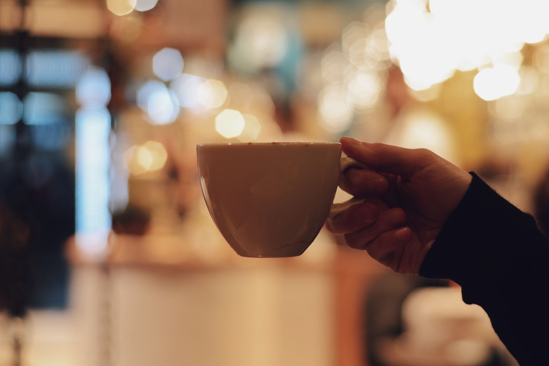 Hand holding a ceramic coffee cup with warm bokeh light — handcrafted goods.